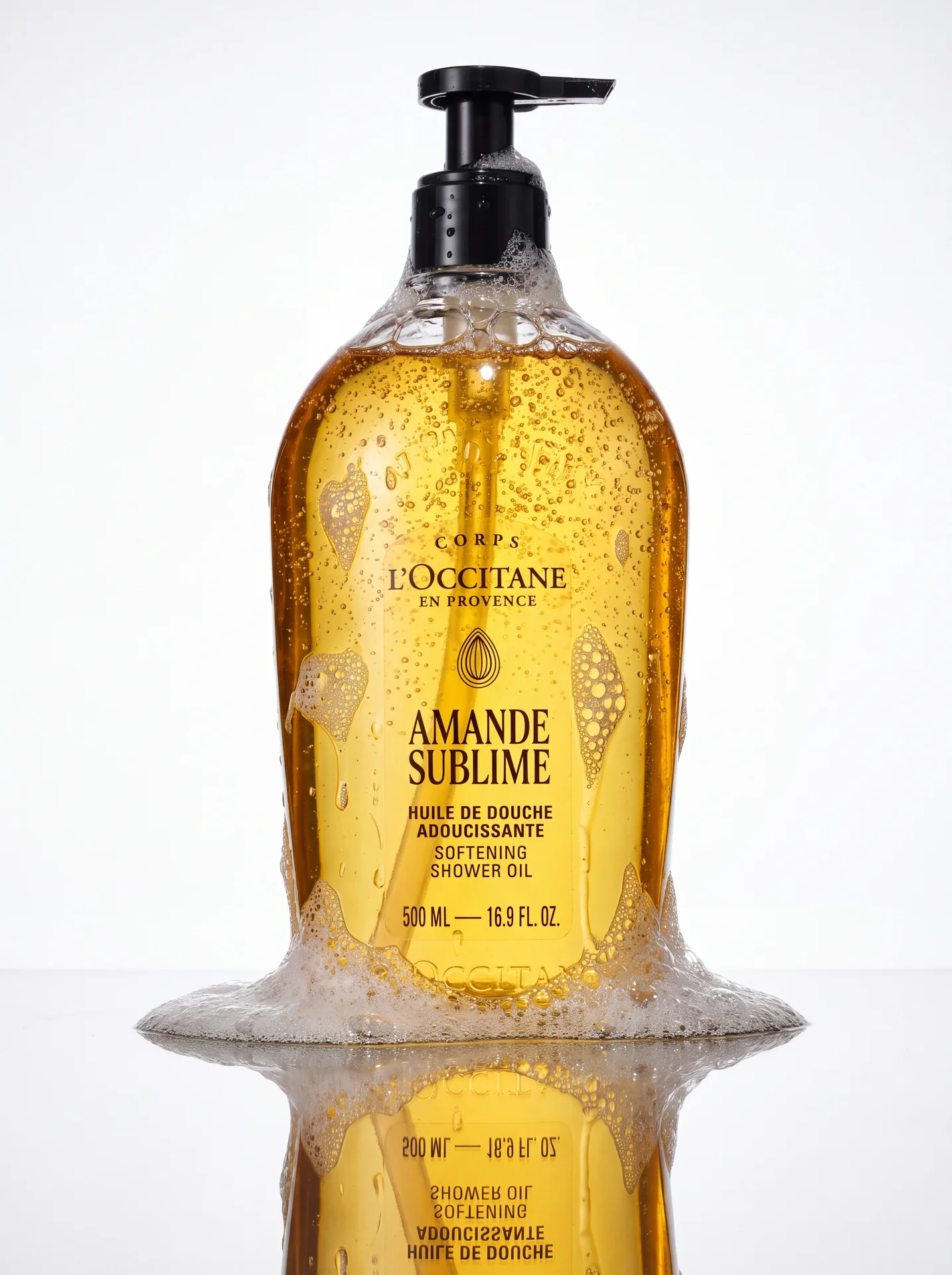 Amande Sublime shower oil bottle standing in a ring of white foam on a white background