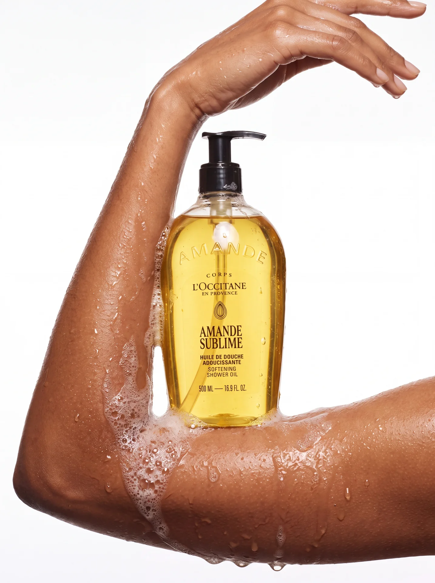 Amande Sublime bottle held in the crook of a raised arm, water droplets on skin
