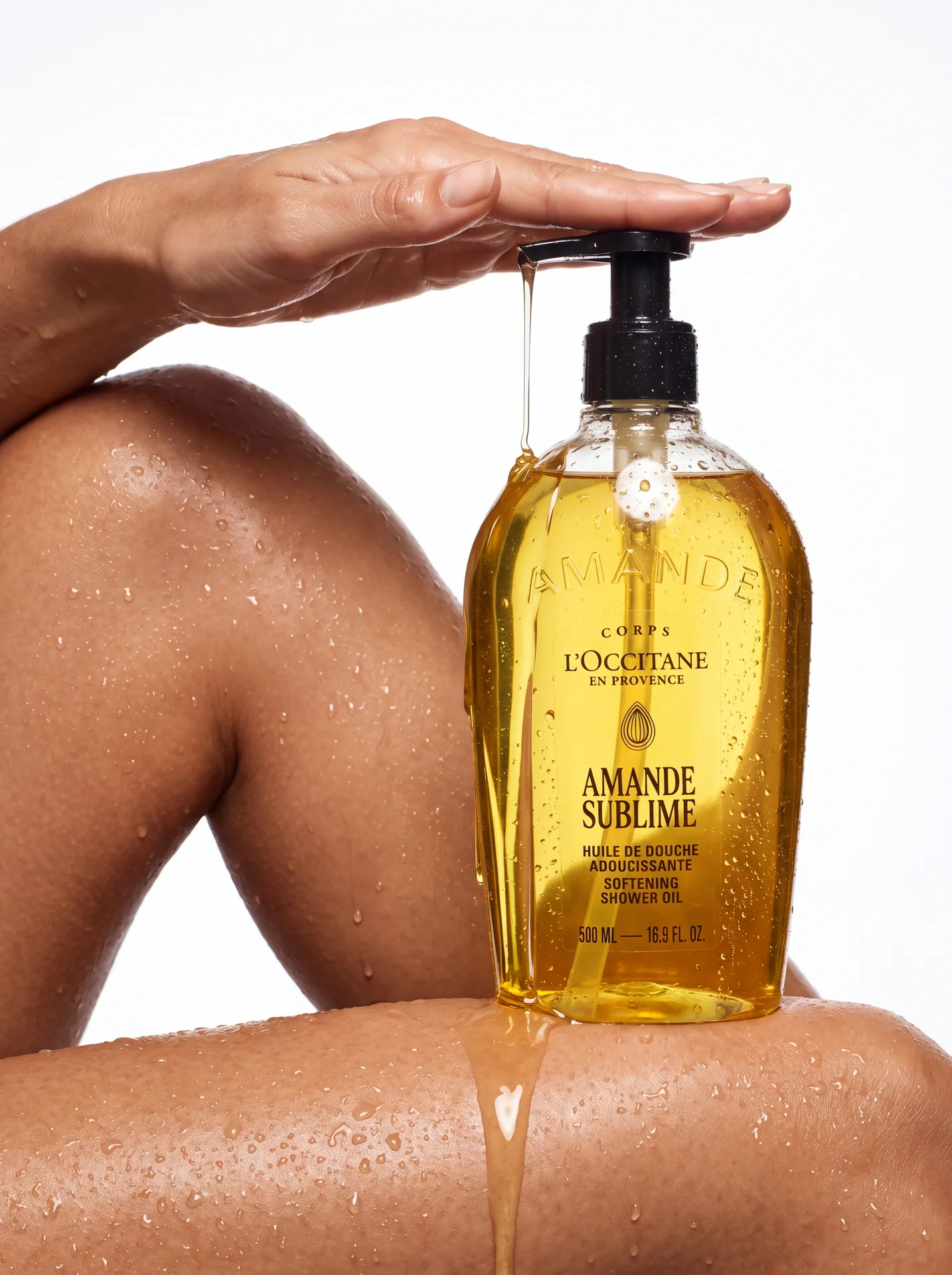 Amande Sublime bottle resting on a wet knee, hand on the pump