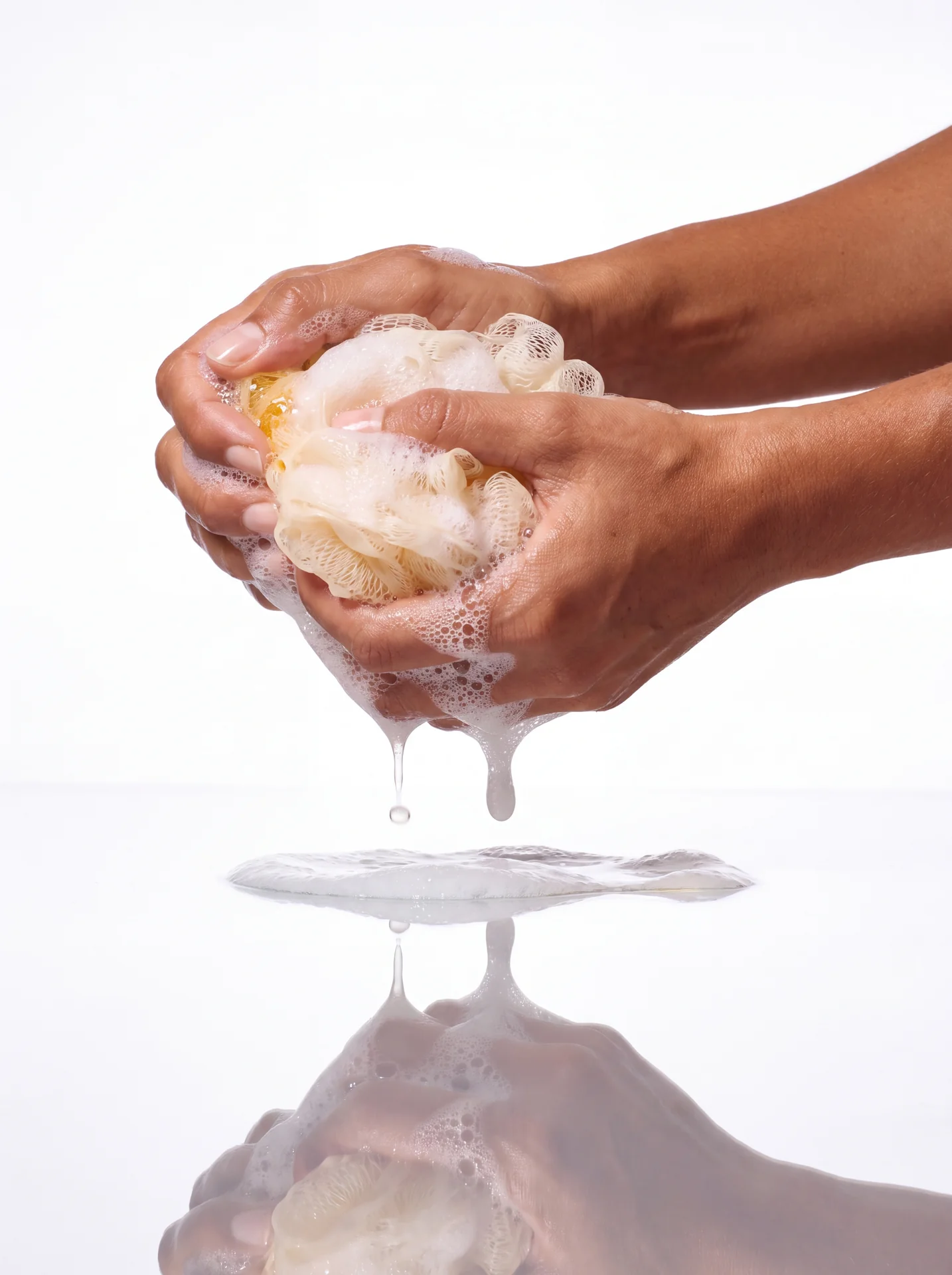 Hands squeezing white lather from a sponge over a mirrored reflection