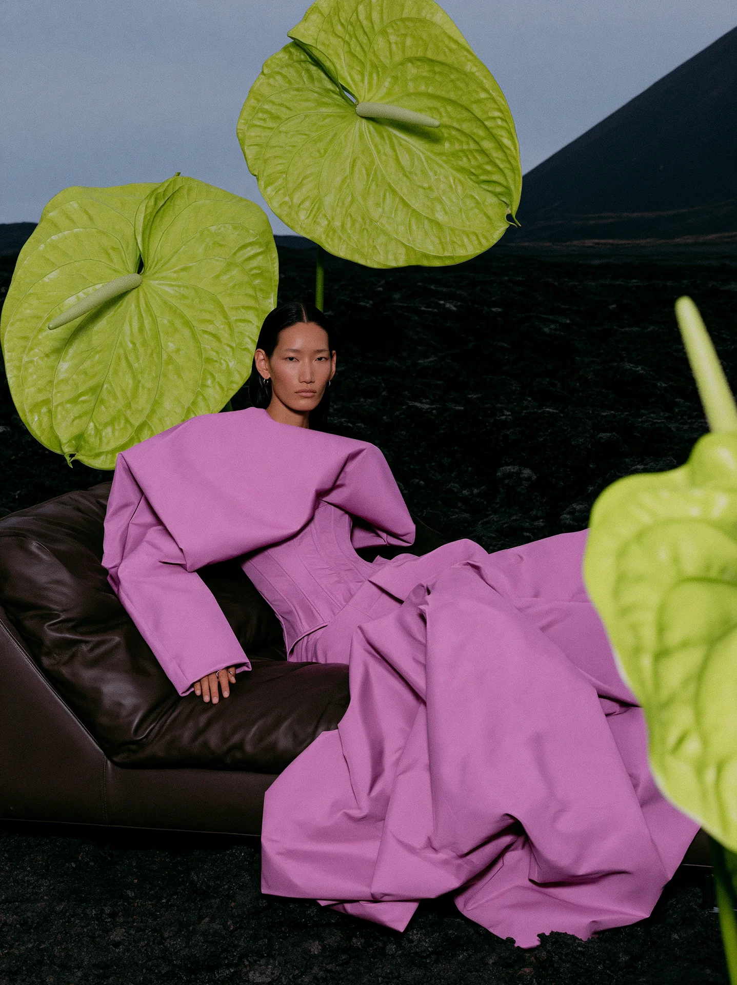 Pink tailored fashion look seated beneath giant green leaves in a dark landscape, a MARSE surreal editorial concept