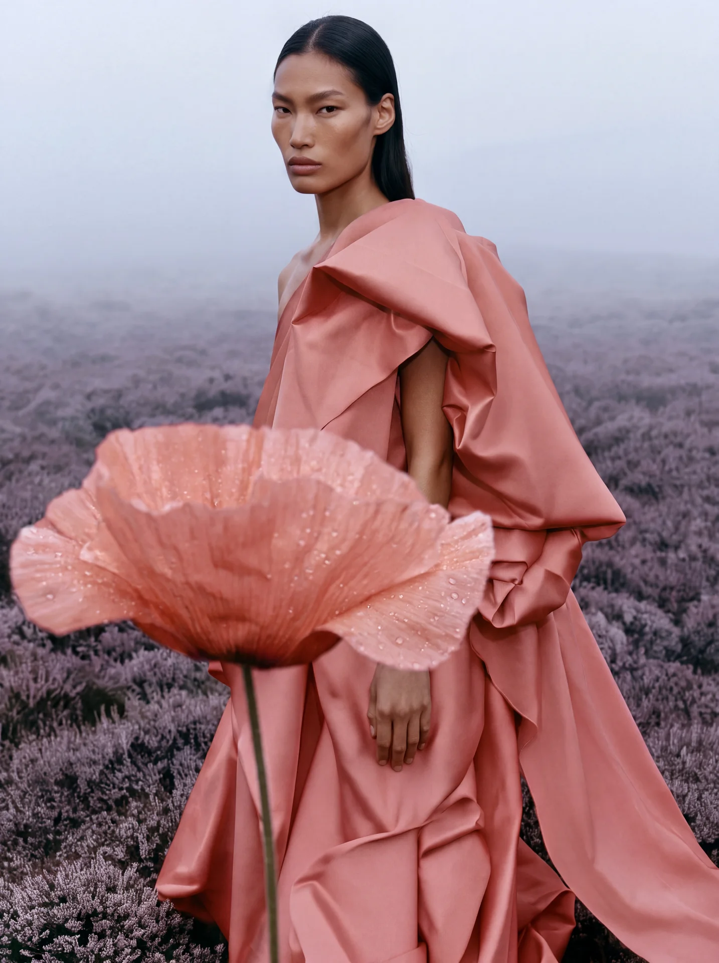 Woman in a pink dress holding an oversized poppy stem at her side